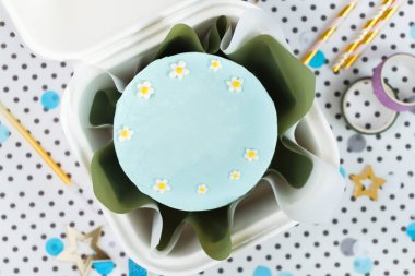 Pastel mavi kremalı küçük bento keki beyaz bir hediye kutusunda krema çiçekleriyle süslenmiş. Beyaz noktalı arka planda düz bir doğum günü pastası..