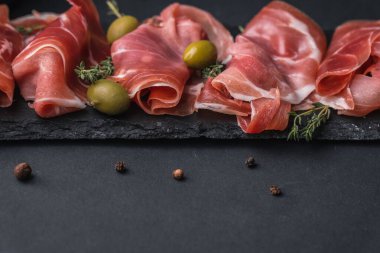 Kurutulmuş Serrano jambonu ya da İspanyol jamonu iberico 'dan aperatifler. İtalyan jambonlu, yeşil zeytinli ve siyah taşlı. Siyah arkaplanda et dilimleri