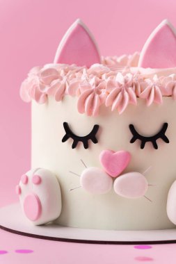 Kedi şeklinde şirin bir doğum günü pastası. Pembe arka planda pembe krem kürkle süslenmiş mastik kulakları ve pençeleri var. Kedileri seven küçük bir kız için sevimli bir pasta.