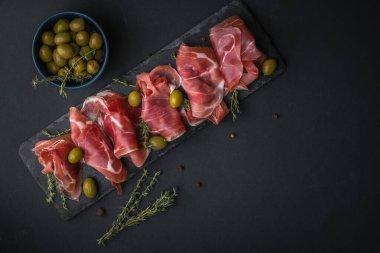 Kurutulmuş Serrano jambonu ya da İspanyol jamonu iberico 'dan aperatifler. İtalyan jambonlu, yeşil zeytinli ve siyah taşlı. Siyah arkaplanda et dilimleri