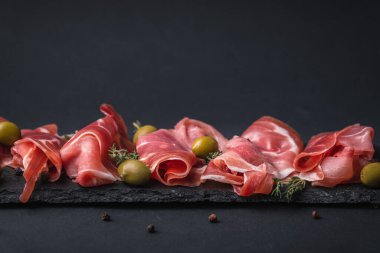 Kurutulmuş Serrano jambonu ya da İspanyol jamonu iberico 'dan aperatifler. İtalyan jambonlu, yeşil zeytinli ve siyah taşlı. Siyah arkaplanda et dilimleri
