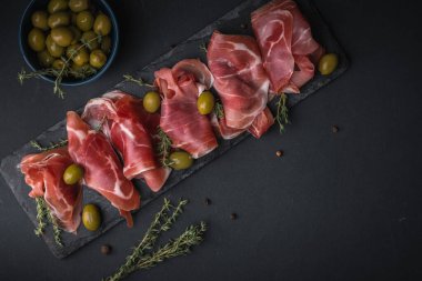 Kurutulmuş Serrano jambonu ya da İspanyol jamonu iberico 'dan aperatifler. İtalyan jambonlu, yeşil zeytinli ve siyah taşlı. Siyah arkaplanda et dilimleri