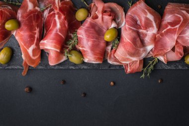 Kurutulmuş Serrano jambonu ya da İspanyol jamonu iberico 'dan aperatifler. İtalyan jambonlu, yeşil zeytinli ve siyah taşlı. Siyah arkaplanda et dilimleri