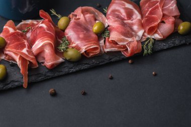 Kurutulmuş Serrano jambonu ya da İspanyol jamonu iberico 'dan aperatifler. İtalyan jambonlu, yeşil zeytinli ve siyah taşlı. Siyah arkaplanda et dilimleri