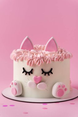 Kedi şeklinde şirin bir doğum günü pastası. Pembe arka planda pembe krem kürkle süslenmiş mastik kulakları ve pençeleri var. Kedileri seven küçük bir kız için sevimli bir pasta.