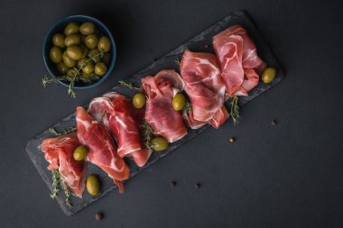 Kurutulmuş Serrano jambonu ya da İspanyol jamonu iberico 'dan aperatifler. İtalyan jambonlu, yeşil zeytinli ve siyah taşlı. Siyah arkaplanda et dilimleri