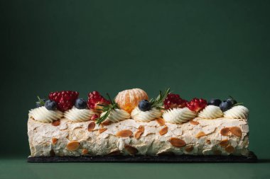 Üzerinde yaban mersini, nar ve badem taneleri ile süslenmiş pudra şekeri serpiştirilmiş kremalı pasta ve bulanık Noel ağacı. Noel pastası