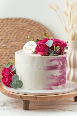 Beyaz krem peynirli pasta ve ahşap tezgahta kırmızı güllerle süslenmiş pembe krema lekeleri.