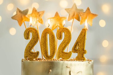 Altın yıldızlarla süslenmiş büyük altın bir yeni yıl pastası ve arka planda Bokeh ışıkları karşısında mumlar. Mutlu yıllar 2024. Kış tatili geçmişi