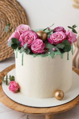 Tahta tezgahta pembe güllerle süslenmiş beyaz çikolata kadife kaplı yıldönümü pastası.