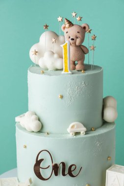 Turkuaz çikolatalı küçük bir çocuk için iki katlı doğum günü pastası. Çikolatalı oyuncak ayı heykelciği ve bulutlarla süslenmiş bir bebek için doğum günü pastası.