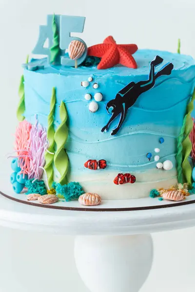 Sea themed summer cake for a mariner with blue chocolate frosting decorated with nautical inhabitants, seaweed and diver on the white background. Birthday cake for a seaman
