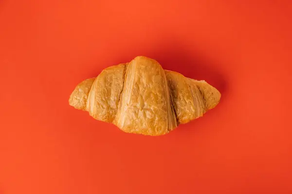 Flat lay of single freshly baked croissant on the red background. Traditional French pastry with a copy space for a free text