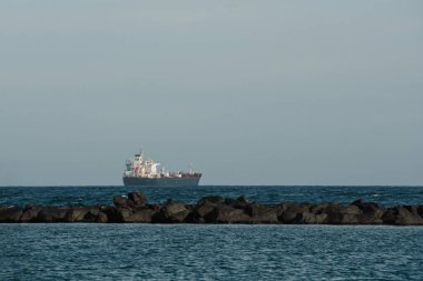 Dalgalar okyanusta dalgalanan sulara çarpıyor ve arka planda bir gemi var. Dalgalar fren yapar ve kayaya çarpar. Uzakta büyük bir gemi ücretsiz metin için bir kopya alanı ile