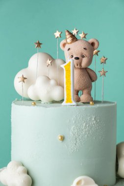 Turkuaz çikolatalı küçük bir çocuk için iki katlı doğum günü pastası. Çikolatalı oyuncak ayı heykelciği ve bulutlarla süslenmiş bir bebek için doğum günü pastası.