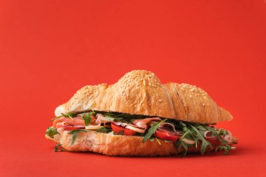 İber jambonlu, domatesli ve kırmızı arka planda salatalı taze pişmiş kruvasan. Ücretsiz metin için kruvasan kopyalama alanı ile modelle