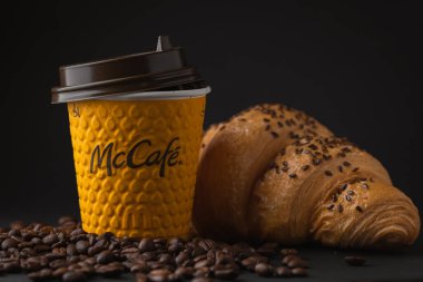 KYIV, UKRAINE - Ocak 06: Popüler bir fast food restoranında taze kruvasanla sarı McDonald 's kağıt bardağına yakın çekim yapın. Siyah arka planda uçan kahve çekirdekleri olan McCafe bardağı.