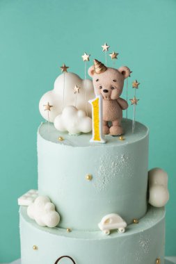Turkuaz çikolatalı küçük bir çocuk için iki katlı doğum günü pastası. Çikolatalı oyuncak ayı heykelciği ve bulutlarla süslenmiş bir bebek için doğum günü pastası.