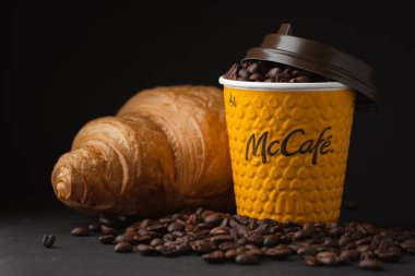 KYIV, UKRAINE - Ocak 06: Popüler bir fast food restoranında taze kruvasanla sarı McDonald 's kağıt bardağına yakın çekim yapın. Siyah arka planda uçan kahve çekirdekleri olan McCafe bardağı.