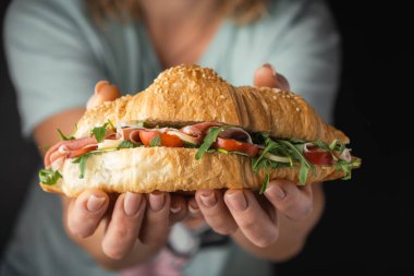 Kadın elleri taze pişmiş kruvasan, İber jambonu, domates ve salata dolgulu. Sağlıklı beslenme konsepti seçimi. Geleneksel Fransız pastası