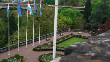 Lüksemburg Bayrakları ve Avrupa Birliği 'nin panoramik görüntüsüyle kayan çekim. Arka planda Alzette Nehri' nin karşısındaki Old Passerelle Köprüsü var.