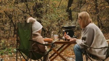 Küçük kızı olan bir anne ormanda piknik yapıyor. Doğada ailecek tatildeyiz. Gazlı ısıtıcının üstünde buharlı tencere. Doğada yemek hazırlıyorum.