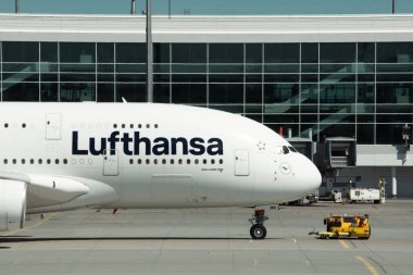 Münih, Almanya - 27 Nisan 2024: Airbus A380 kabin ve burun teçhizatı ile Münih Havalimanı 'ndaki Lufthansa havayolları. Terminal binasının yanında büyük yolcu uçağı ve çekici var.