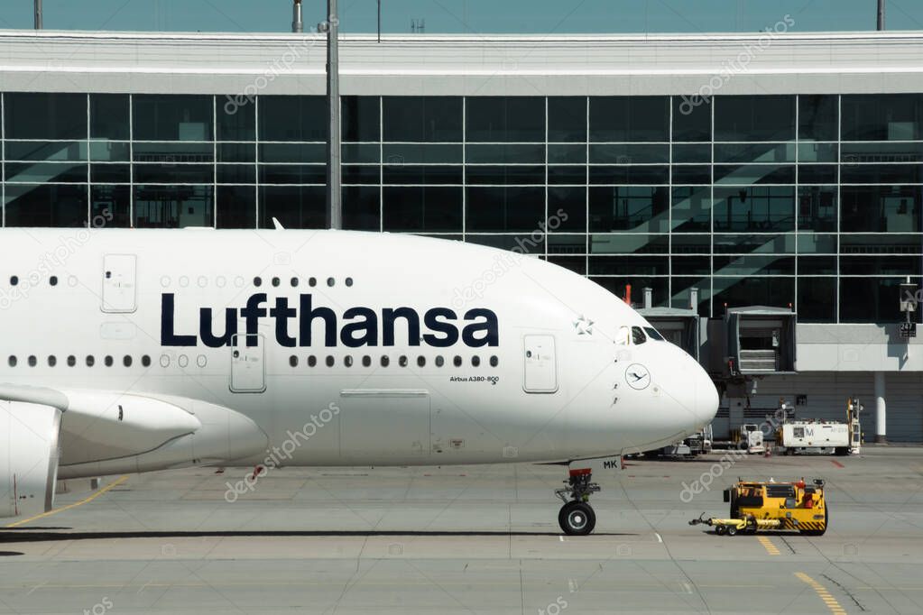 Munich, Germany - April 27, 2024: Close up of Airbus A380 cabin and nose gear with livery of Lufthansa airlines at Munich Airport. Big passenger aircraft and towing truck next to terminal building