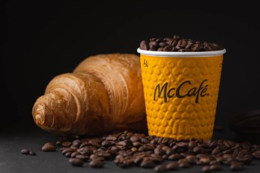 KYIV, UKRAINE - Ocak 06: Popüler bir fast food restoranında taze kruvasanla sarı McDonald 's kağıt bardağına yakın çekim yapın. Siyah arka planda uçan kahve çekirdekleri olan McCafe bardağı.