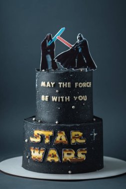 Kyiv, Ukraine - May 17, 2024: Star Wars two tier birthday cake with black chocolate frosting decorated with edible mastic Darth Vader vs Obi-Wan silhouettes fighting with red and blue Lightsabers clipart