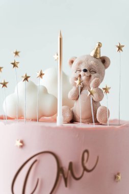 Oyuncak ayı ve beyaz bulutlarla süslenmiş pembe çikolata kaplı küçük bir bebek için doğum günü pastası. Beyaz arka planda küçük bir kız için doğum günü pastası