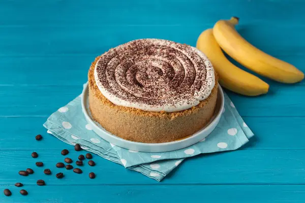 stock image Banoffe pie filled with banana and dulce de leche and sprinkled with grated chocolate. Banana cake on white plate with glass of coffee on turquoise summer background