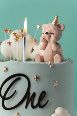 Oyuncak ayı ve beyaz bulutlarla süslenmiş turkuaz çikolata kaplı küçük bir bebek için doğum günü pastası. Turkuaz arka planda küçük bir çocuk için bebek partisi pastası.