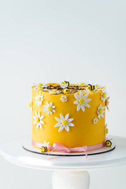 Yenebilir şeker ezmesi arıları ve beyaz papatya çiçekleri ile süslenmiş sarı çikolatalı bahar pastası. Beyaz arkaplan