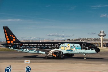 Madrid, Spain - February 02, 2024: Big passenger Airbus A320 aircraft of Brussels Airlines with Tintin comics Livery taxing by Air Traffic Control Tower in Madrid-Barajas Airport during sunny day. clipart