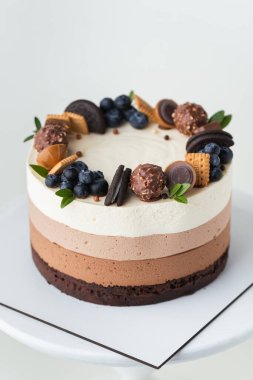 Sünger bisküvili çikolatalı sufle keki ve beyaz arka planda kurabiye, şeker ve yabanmersinli üç çikolatalı krema katmanı.