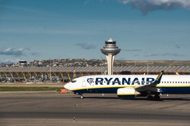 Madrid, İspanya - 2 Şubat 2024: Güneşli bir günde Madrid-Barajas Havaalanı 'ndaki hava trafik kontrol kulesinin yanında düşük maliyetli Ryanair Airlines' ın büyük yolcu uçağı Boeing 737-8AS