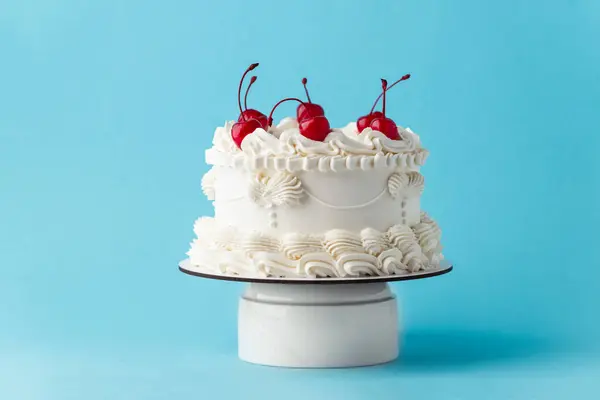 stock image Delicate lambeth style birthday cake with white cream cheese frosting decorated with cocktail cherries on the blue background