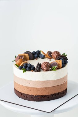 Sünger bisküvili çikolatalı sufle keki ve beyaz arka planda kurabiye, şeker ve yabanmersinli üç çikolatalı krema katmanı.