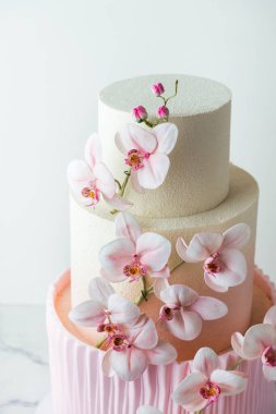Pembe orkide çiçekleriyle süslenmiş kadife çikolata kaplı üç katlı güzel bir pasta. Beyaz arka planda düğün pastası