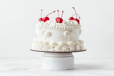 Beyaz arka planda kokteyl kirazlarıyla süslenmiş beyaz krem peynirli Lambeth tarzı doğum günü pastası.