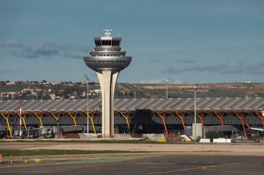 Madrid, Spain - February 12, 2024: Big and modern Air traffic control tower near the terminal building in Madrid-Barajas Airport during sunny day. clipart