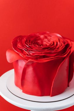 Kırmızı arka planda kırmızı şeker macunu gül yapraklarıyla süslenmiş gül goncası şeklinde güzel bir yıldönümü pastası.