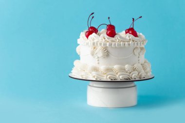 Delicate lambeth style birthday cake with white cream cheese frosting decorated with cocktail cherries on the blue background clipart