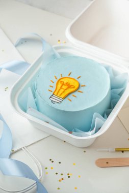 Flat lay of a cute little Korean style cake in a gift bento box with blue cream cheese frosting decorated with yellow light bulb silhouette drawing. Bright birthday cake clipart