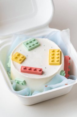 Hediye kutusunda küçük bir lego tarzı pasta. Beyaz arka planda renkli çikolata yapı taşlarıyla süslenmiş doğum günü pastası