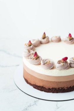 Beyaz mermer arka planda ev yapımı üç çikolata. Süngerli çikolatalı sufle kek ve çırpılmış krema ve kurutulmuş çiçeklerle süslenmiş üç kat çikolatalı mus.