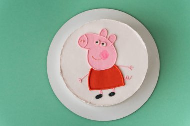 Kyiv, Ukrayna - 09 Kasım 2024: Turkuaz arka planda Peppa Pig doğum günü pastası. Komik pembe domuzla süslenmiş küçük bir çocuk için tatlı bir pasta.