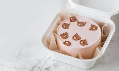 Little birthday bento cake with pink cream cheese frosting in a gift box decorated with cute cream teddy bear faces. Birthday cake for a girl on the white marble background clipart