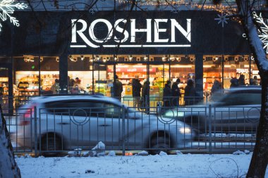 Boryspil, Ukrayna - 15 Aralık 2024: Ön planda araba trafiği olan Roshen şekerleme dükkanının kış gecesi görüntüsü. Karlı havalarda Ukrayna 'da popüler şekerci dükkanının parlak pencereleri
